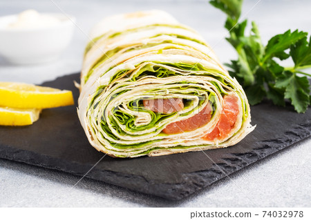 Rolls of thin pita bread and red salted salmon with lettuce leaves On a slate stand, grey concrete background. Copy space. Rolls of thin pita bread and red salted salmon with lettuce leaves On a slate stand, grey concrete background. Copy space. 74032978