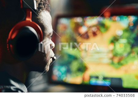 Close up shot of a focused african guy, professional cybersport gamer wearing headphones playing online video games Close up shot of a focused african guy, professional cybersport gamer wearing headphones playing online video games 74033508