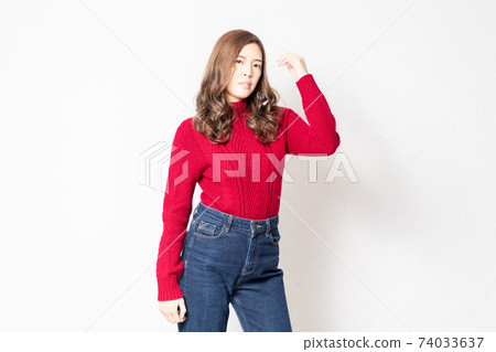 A young woman in a red sweater standing in front of a white wall and posing A young woman in a red sweater standing in front of a white wall and posing 74033637