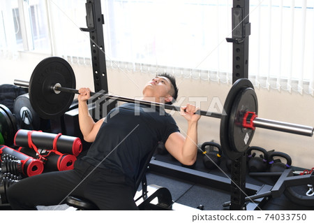 Macho man giving a bench press at the gym Macho man giving a bench press at the gym 74033750