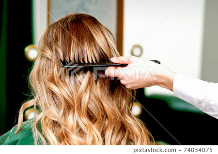Hairdresser combing wavy hair of woman Hairdresser combing wavy hair of woman 74034075