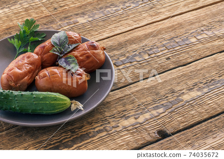 Grilled sausages and cucumber on plate and wooden boards. 74035672