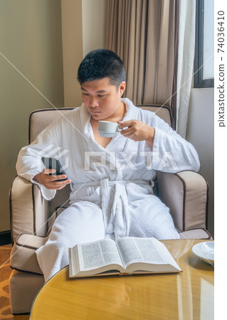 Young Asian businessman wearing bathrobe and using smartphone in hotel 74036410