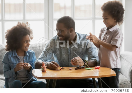 Happy African American father and kids playing with colorful plasticine Happy African American father and kids playing with colorful plasticine 74036788