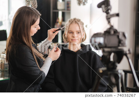 Woman make makeup for attractive blond hair woman in studio. Video of makeup artist applying cosmetics for beautiful model Woman make makeup for attractive blond hair woman in studio. Video of makeup artist applying cosmetics for beautiful model 74038267