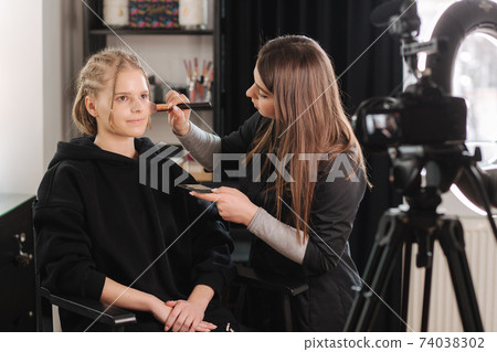 Woman make makeup for attractive blond hair woman in studio. Video of makeup artist applying cosmetics for beautiful model 74038302
