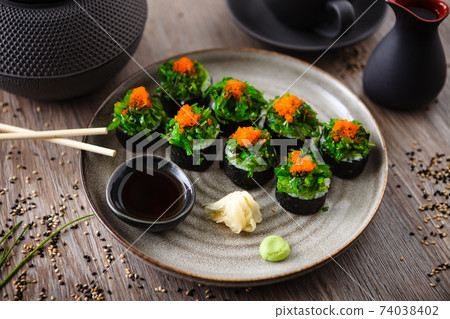 Sushi maki rolls with crab, seaweed salad and flying fish roe on a plate with chopsticks, soy sauce, wasabi and ginger. Japanese traditional seafood served for lunch in modern gourmet restaurant 74038402