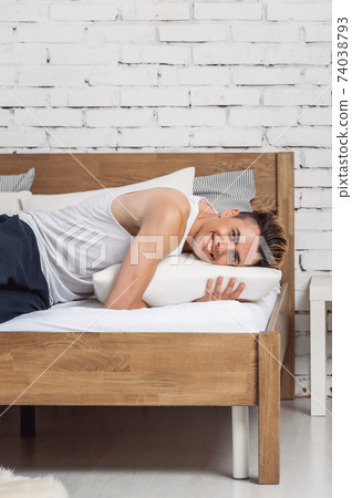 Smiling man lying on a white pillow and a mattress on a wooden bed. Concept of comfortable sleep. orthopedic mattress and pillow Smiling man lying on a white pillow and a mattress on a wooden bed. Concept of comfortable sleep. orthopedic mattress and pillow 74038793