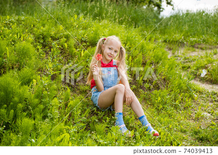 Blonde little girl with long hair and candy on a stick 74039413