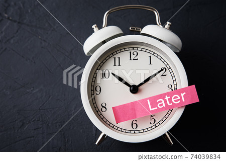 Procrastination and delay concept. Sticky note with word later on white alarm clock. Urgency time Procrastination and delay concept. Sticky note with word later on white alarm clock. Urgency time 74039834