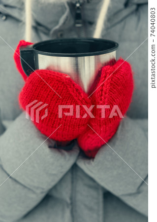 hands in red mittens holding a cup of tea 74040803
