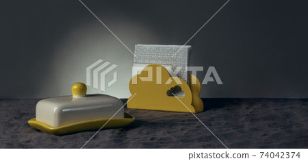 Still life of an oilcan and a yellow napkin holder with white napkins on a tablecloth made of gray natural linen Still life of an oilcan and a yellow napkin holder with white napkins on a tablecloth made of gray natural linen 74042374