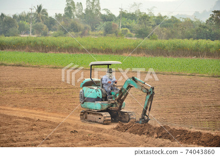 Gardeners are forcing a small loader to dig a garden trench with tree background. Gardeners are forcing a small loader to dig a garden trench with tree background. 74043860