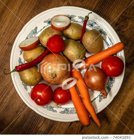 Raw vegetables on a plate. Potatoes, onions, tomatoes, carrots, hot red peppers. 74043891