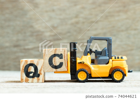 Toy forklift hold letter block C to complete word QC (Abbreviation of Quality Control) on wood background Toy forklift hold letter block C to complete word QC (Abbreviation of Quality Control) on wood background 74044621