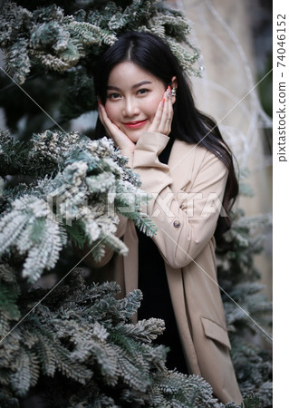 Portrait of young beautiful woman in winter clothes. while posing on snow background. Outdoor close-up photo of female model with romantic smile chilling in park in winter. 74046152