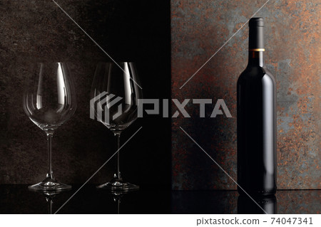 Bottle of red wine with empty wine glasses on rusty brown background. Bottle of red wine with empty wine glasses on rusty brown background. 74047341