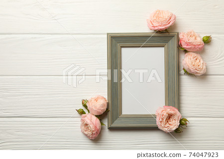Roses and blank frame on white wooden background 74047923