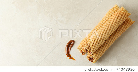 Tasty wafer rolls with condensed milk on white textured background Tasty wafer rolls with condensed milk on white textured background 74048956