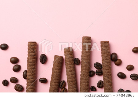 Chocolate wafer rolls and coffee beans on pink background Chocolate wafer rolls and coffee beans on pink background 74048963