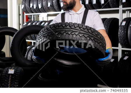 confident caucasian car mechanic in a workshop on a stack of tires at his workplace confident caucasian car mechanic in a workshop on a stack of tires at his workplace 74049335