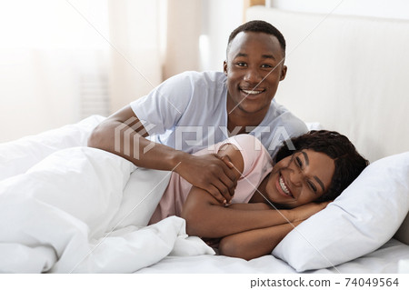 Happy black couple cuddling in bed at home Happy black couple cuddling in bed at home 74049564