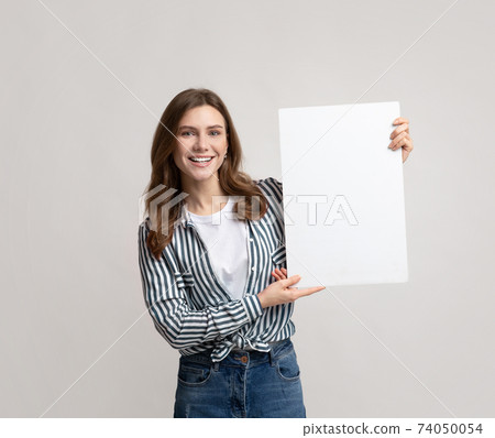 Cheerful Young Woman With Blank Placard In Hands STanding Over Gray Background 74050054