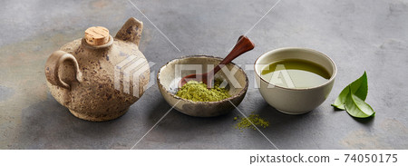 Green matcha powder with leaves and clay tea pot on graphite background 74050175