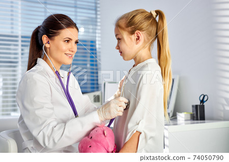 caucasian female doctor or pediatrician with stethoscope listening to girl's patient on medical exam at clinic 74050790