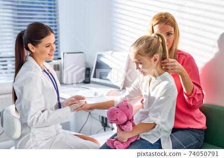 friendly young caucasian doctor talking to child and his mother during health checkup at the clinic 74050791