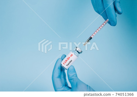 Doctor injecting vial dose of COVID-19 vaccine with syringe against blue background with copy space - prevention coronavirus, global vaccination concept. Selective focus Doctor injecting vial dose of COVID-19 vaccine with syringe against blue background with copy space - prevention coronavirus, global vaccination concept. Selective focus 74051366