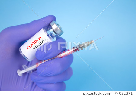 Doctor or scientist holding vial dose of COVID-19 vaccine with syringe against blue background with copy space - prevention coronavirus, global vaccination concept. Selective focus Doctor or scientist holding vial dose of COVID-19 vaccine with syringe against blue background with copy space - prevention coronavirus, global vaccination concept. Selective focus 74051371