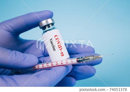Doctor or scientist holding vial dose of Covid-19 vaccine with syringe against blue background with copy space - prevention coronavirus, global vaccination concept. Selective focus 74051378