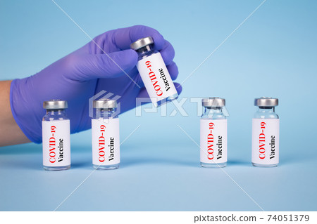 Doctor or scientist holding vial dose of Covid-19 vaccine against blue background with copy space - prevention coronavirus, global vaccination concept. Selective focus Doctor or scientist holding vial dose of Covid-19 vaccine against blue background with copy space - prevention coronavirus, global vaccination concept. Selective focus 74051379