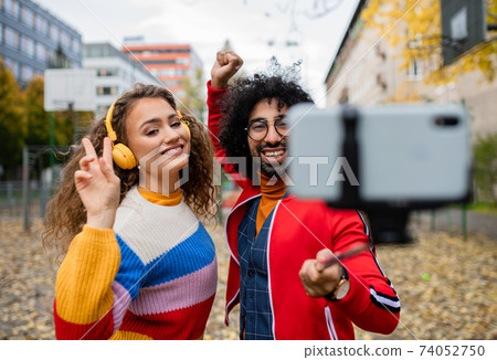 Young couple with smartphone making video for social media outdoors in city park. 74052750