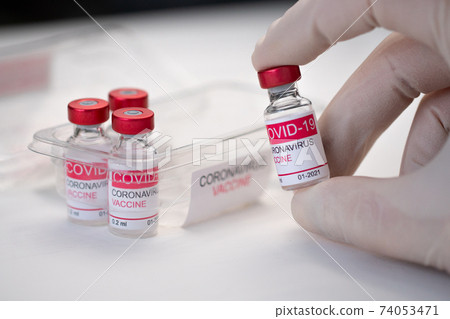 Closeup doctor hand holding a glass bottle of coronavirus vaccine. Concept of coronavirus vaccination. Macro Closeup doctor hand holding a glass bottle of coronavirus vaccine. Concept of coronavirus vaccination. Macro 74053471