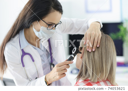 Otorhinolaryngologist examining patients sore ear with otoscope in clinic 74053621