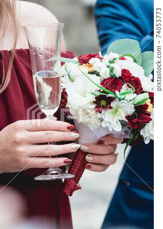 girl in a pomegranate dress and with red manicure holding in her hands glass with champagne 74053773