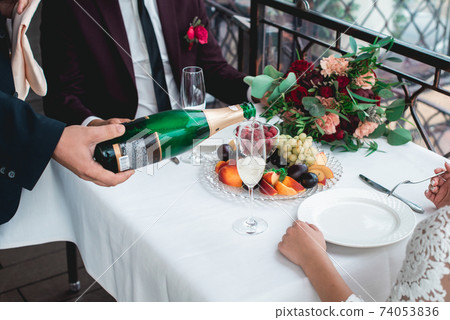 Waiter pouring wine into glass. Happy newlyweds drinking. Loving couple created new family. Waiter pouring wine into glass. Happy newlyweds drinking. Loving couple created new family. 74053836