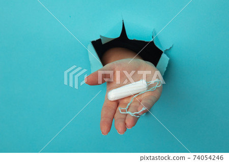 Female hand holds cotton tampon through torn paper background, health care concept Female hand holds cotton tampon through torn paper background, health care concept 74054246