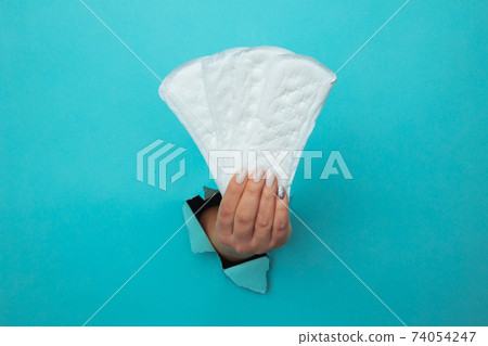 Female hand holds daily sanitary pads through torn blue paper background Female hand holds daily sanitary pads through torn blue paper background 74054247