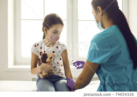 Doctor is about to inject a vaccine into the hand of a cute little girl holding her favorite toy. 74054326