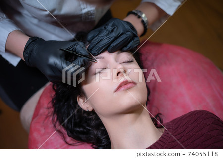 beautiful female at beautician on eyebrows correction procedure with tweezers beautiful female at beautician on eyebrows correction procedure with tweezers 74055118