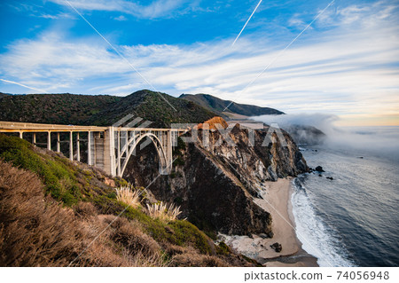 Bixby bridge foggy sunset landscape in Big Sur area on the California coast with ocean waters crashing on the shore. 74056948