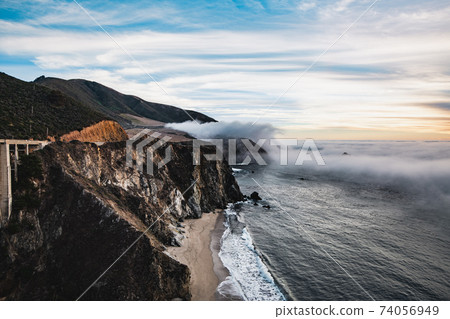 Scenic view of ocean shore near Big Sur, California, USA. Cloud covered coast, sea and cliff hills. Foggy pink sunset landscape. 74056949