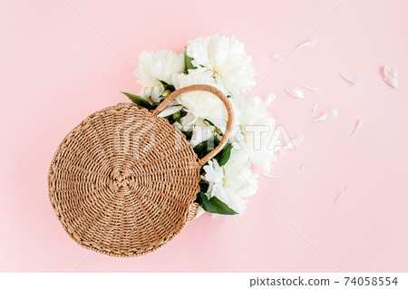 White bouquet of peonies in a straw bag on pink background. Minimal floral concept greeting card. Flat lay, top view.  74058554