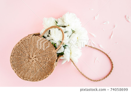 White bouquet of peonies in a straw bag on pink background. Minimal floral concept greeting card. Flat lay, top view. White bouquet of peonies in a straw bag on pink background. Minimal floral concept greeting card. Flat lay, top view. 74058699