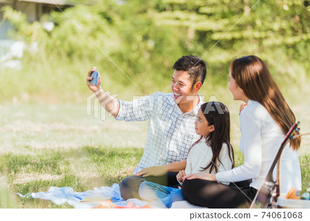 Happy family having fun outdoor sitting on picnic blanket taking selfie 74061068