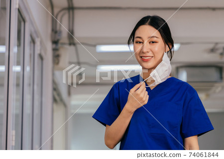 Young beautiful Asian medical nurse in scrub uniform at hospital prepared to wear a face mask. Professional medic at workplace during Covid19 pandemic 74061844