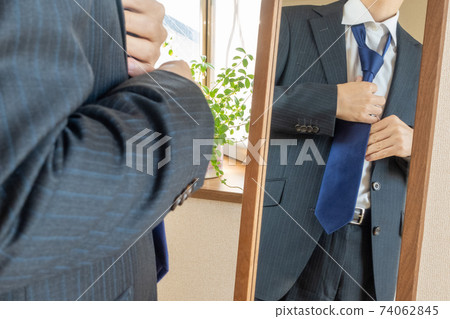 A grooming check image of a businessman in a suit wearing a tie in front of a mirror 74062845